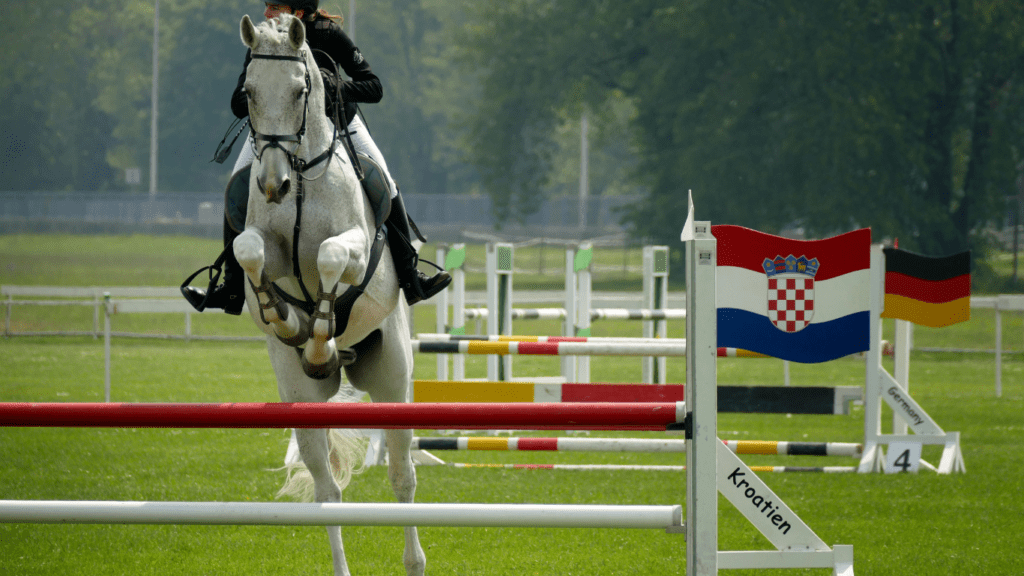 a rider on a white horse jumping over an obstacle